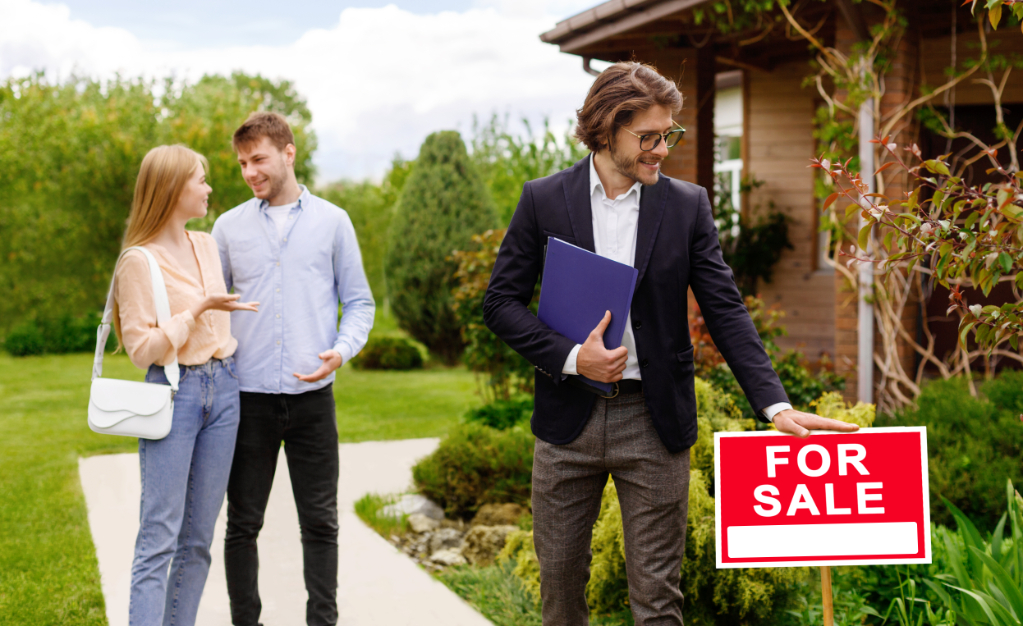 Real estate agent near FOR SALE tablet and would-be home owners near beautiful house outdoors